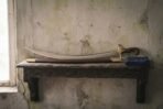 Curved steel shamshir sword with brass quillons and wooden grip resting on its scabbard on a carved wall shelf