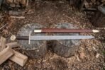 Damascus arming sword and brown leather scabbard with brass fittings laid across two stumps in a wood yard