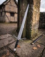 Damascus arming sword with a black grip and wheel pommel standing against a stone column, black scabbard on flagstones, timber house behind