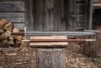 Damascus arming sword with brass guard and disc pommel resting on a log beside its brown leather scabbard