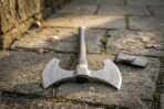 Damascus double bit war axe head close up with engraved knotwork and rune bands, lying on stone paving by its cover