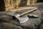 Damascus double bit war axe on a dark wooden haft with brass collar, lying across old stone paving beside a leather cover