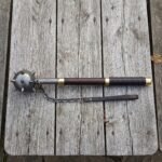 Damascus flail with a forge welded spiked ball head, brass collars, rosewood haft and hanging chain laid on a silvered timber table top