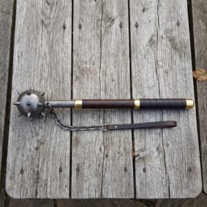 Damascus flail with a forge welded spiked ball head, brass collars, rosewood haft and hanging chain laid on a silvered timber table top