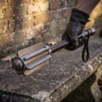 Damascus flanged mace with polished collars held in a black gloved hand over a stone bench by a brick wall