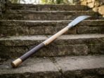 Damascus glaive resting on old stone steps with its cord wrapped grip and brass butt cap in the foreground