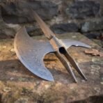 Damascus halberd head seen from the side showing crescent blade, rear hook and split langets on weathered stone