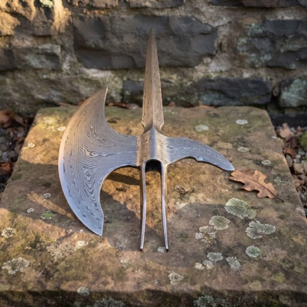 Damascus halberd head with a forge welded spike, patterned crescent blade and twin langet straps standing upright on a lichen covered stone slab