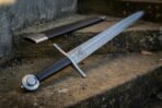 Damascus hand and a half sword with Valknut etch and wheel pommel lying across a step near its black scabbard