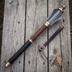 Damascus mace with six forge welded flanges, brass collars and a rosewood haft lying on a silvered timber table beside a buckled leather wrist strap
