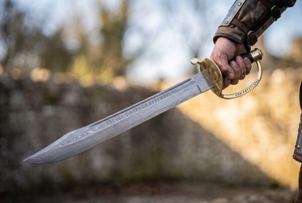 Damascus naval cutlass with brass shell guard held blade out against a blurred castle wall in low winter sun