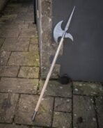 Damascus pattern halberd leaning on a stone pillar above flagstones, leather head cover resting at the foot