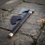 Damascus steel bearded axe with a dark leather wrapped haft, brass collar and brass pommel cap, laid on stone paving with its sheath