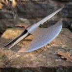 Damascus steel halberd head with crescent axe blade, top spike and twin langet straps resting on a sandstone slab