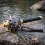 Damascus steel morning star mace with pyramid spikes, brass collars and dark haft resting on a riverside rock with a wrist strap