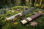 Damascus Viking seax with antler grip and brass pommel, closer angled view on a mossy rock with oak leaves and the sheath