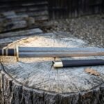 Damascus Viking sword with dark etched layered steel blade and black leather scabbard resting on a weathered tree stump in a wooded clearing