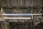 Elven longsword and its pale cream scabbard resting on a worn stone step, showing the polished fuller inscription and ribbed leather wrapped grip