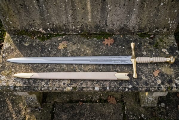 Elven longsword and its pale cream scabbard resting on a worn stone step, showing the polished fuller inscription and ribbed leather wrapped grip