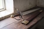 Espada ropera with blackened swept hilt and brass pommel lying on a window ledge beside its brass mounted leather scabbard