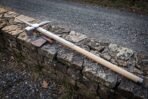 Forged polehammer on an ash haft with steel langets and butt cap resting diagonally on a dry stone wall beside its leather head cover