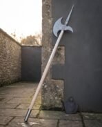 Full length Damascus halberd with ash shaft and steel butt cap propped against a dark wall corner with its leather head cover