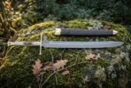 Full length Damascus langes messer and black leather scabbard with brass mounts laid out on a mossy boulder