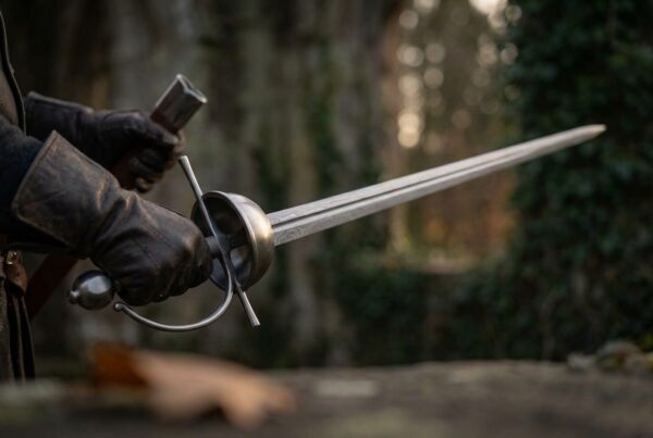 Gloved hand holding a Damascus rapier with steel cup hilt and knuckle bow, blade pointing across a dark courtyard
