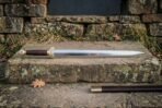Hand forged Chinese jian sword with a straight polished double edged blade and brass ferruled grip resting on a sandstone step below a dry stone wall