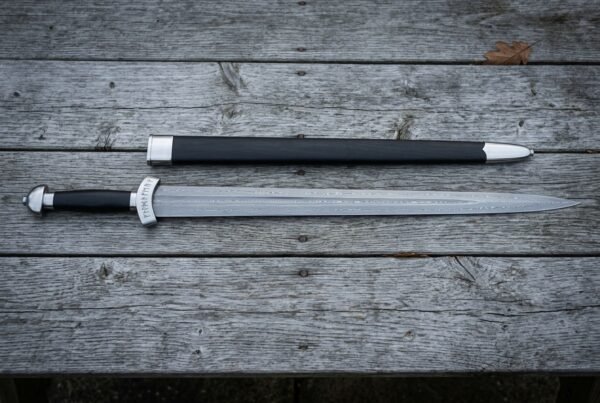 Hand forged Damascus Chinese sword with a straight layered double edged jian blade and wrapped grip lying on weathered timber decking beside a black scabbard