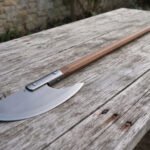 Hand forged high carbon steel bardiche with crescent blade and hardwood haft, angled view of the head on a wooden table