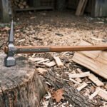 Hand forged high carbon steel medieval war hammer with spiked head and wooden haft, resting on a stump among wood chips