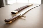 Hand forged high carbon steel shamshir with brass pommel cap and wooden grip, close view of the hilt and scabbard on a table