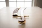 Hand forged high carbon steel shamshir with deeply curved blade, low angle view of sword and scabbard on a table