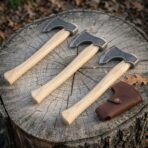 Hand forged high carbon steel Viking throwing axe set of three with wooden handles, angled view on a stump by a sheath