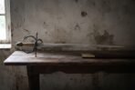 Hand forged italian rapier with a blackened swept hilt and gilt brass finials resting on a dark timber table against a cracked plaster wall