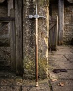 Hand forged medieval polehammer with a steel hammer head and top spike on a walnut haft with brass langets leaning against a weathered stone pier