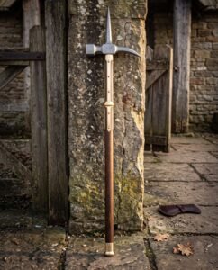 Hand forged medieval polehammer with a steel hammer head and top spike on a walnut haft with brass langets leaning against a weathered stone pier