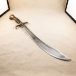 Hand forged scimitar with a satin finished 1095 steel blade, brass quillons and riveted hardwood grip, photographed on a pale sand coloured canvas backdrop