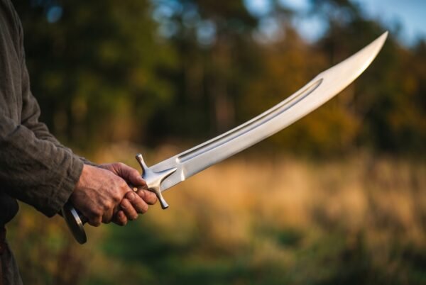 Hand forged tulwar with deep curved fullered blade and steel disc pommel held out in a field at sunset