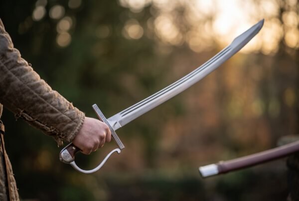Hand swinging a curved steel pirate cutlass with knuckle bow guard against a blurred sunset forest