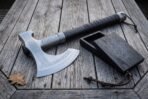 High carbon steel bearded axe with rune engraved head and dark leather wrapped haft beside a small knotwork inlaid wooden box