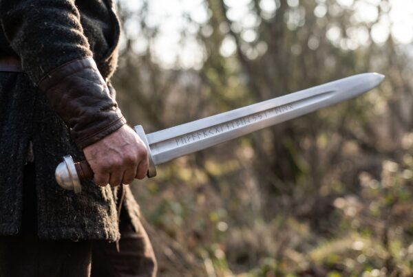 High carbon steel falchion with wooden grip and steel pommel held low in one hand against a wintry woodland background