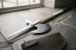 High carbon steel halberd head with spike, crescent blade and brass langets lying on a stone sill beside a leather cover