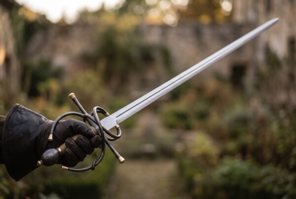 Italian rapier with blackened swept hilt held in a gloved hand, the long polished blade pointing over a garden