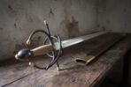 Italian rapier with blackened swept hilt lying beside its dark leather scabbard with brass throat on a wooden table