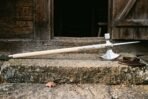 Long poleaxe with a crescent axe head and spike laid across a stone doorstep, a brown leather cover beside the head