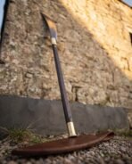 Medieval glaive with blackened curved blade and brass fittings on a dark wooden haft, leather blade cover at the base