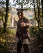 Medieval polehammer with a steel hammer head, curved back spike and brass langets on a dark wood haft held by a man in a padded jacket