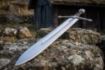 Polished arming sword with fullered blade, curved crossguard and disc pommel resting on a lichen covered stone wall